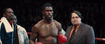 Movie still from “Bleed for This” (2016), directed by Ben Younger – A man in a boxing ring wearing red boxing gloves; Medium shot, Over the shoulder angle