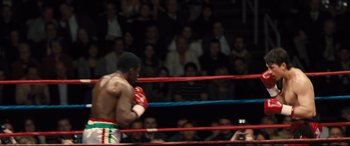 Movie still from “Bleed for This” (2016), directed by Ben Younger – A man in a boxing ring with his hands in the air; Medium shot, Over the shoulder angle