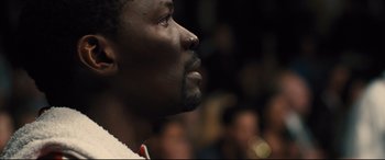 Movie still from “Bleed for This” (2016), directed by Ben Younger – A man's face in front of a group of people; Close Up shot, Over the shoulder angle