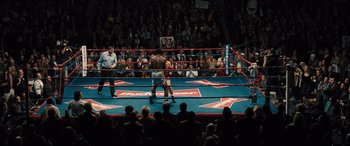 Movie still from “Bleed for This” (2016), directed by Ben Younger – A boxing match in a boxing ring in front of an audience; Extreme Wide shot, Overhead angle
