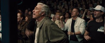 Movie still from “Bleed for This” (2016), directed by Ben Younger – An older man standing in front of a crowd of onlookers; Medium shot, Over the shoulder angle