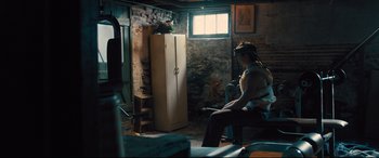 Movie still from “Bleed for This” (2016), directed by Ben Younger – A man sitting in a room next to an old refrigerator; Wide shot, Low angle