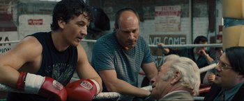 Movie still from “Bleed for This” (2016), directed by Ben Younger – Three men in a boxing ring talking to each other; Medium shot, Over the shoulder angle