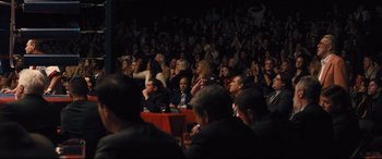 Movie still from “Bleed for This” (2016), directed by Ben Younger – A group of people sitting in front of an audience at an event; Wide shot, Over the shoulder angle