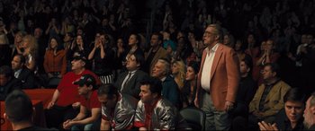 Movie still from “Bleed for This” (2016), directed by Ben Younger – A group of people sitting in front of an audience at an event; Wide shot, High angle