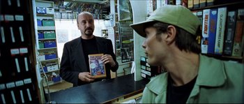 Movie still from “Bleeder” (1999), directed by Nicolas Winding Refn – A man holding up a comic book while another man looks on; Medium shot, Over the shoulder angle