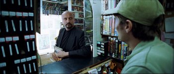 Movie still from “Bleeder” (1999), directed by Nicolas Winding Refn – A man sitting at a counter in a store; Medium shot, Over the shoulder angle