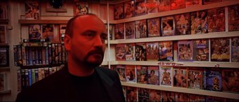 Movie still from “Bleeder” (1999), directed by Nicolas Winding Refn – A man standing in front of a wall covered in dvds; Close Up shot, Low angle