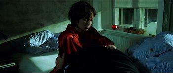 Movie still from “Bleeder” (1999), directed by Nicolas Winding Refn – A woman in a red robe is holding a black bag; Medium shot, High angle