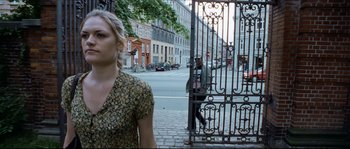 Movie still from “Bleeder” (1999), directed by Nicolas Winding Refn – A woman walking down a street past an iron gate; Medium shot, Over the shoulder angle