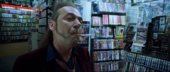 Movie still from “Bleeder” (1999), directed by Nicolas Winding Refn – A man smoking a cigarette in front of a shelf of movies; Close Up shot, Low angle