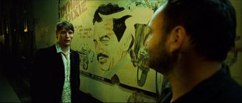 Movie still from “Bleeder” (1999), directed by Nicolas Winding Refn – Two men standing in front of a painting of a man; Medium shot, Over the shoulder angle