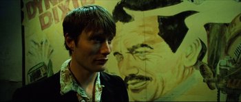 Movie still from “Bleeder” (1999), directed by Nicolas Winding Refn – A man standing in front of a painting of a man; Close Up shot, Low angle