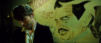 Movie still from “Bleeder” (1999), directed by Nicolas Winding Refn – A man standing in front of a painting of a man; Close Up shot, Low angle