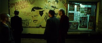 Movie still from “Bleeder” (1999), directed by Nicolas Winding Refn – Two men are standing in front of a poster; Medium shot, Over the shoulder angle