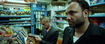 Movie still from “Bleeder” (1999), directed by Nicolas Winding Refn – Two men in suits and ties are looking at a magazine; Medium shot, Low angle