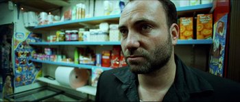 Movie still from “Bleeder” (1999), directed by Nicolas Winding Refn – A person wearing a black shirt in front of shelves; Close Up shot, Low angle