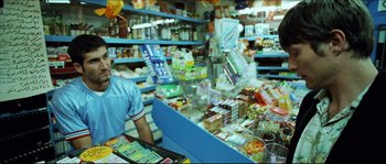 Movie still from “Bleeder” (1999), directed by Nicolas Winding Refn – A man is standing behind a counter in a grocery store; Medium shot, Over the shoulder angle
