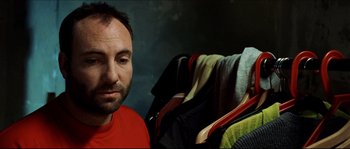 Movie still from “Bleeder” (1999), directed by Nicolas Winding Refn – A person wearing a red shirt near a pile of clothes; Close Up shot, Over the shoulder angle