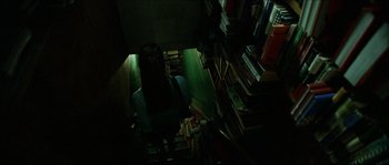 Movie still from “Bleeder” (1999), directed by Nicolas Winding Refn – A woman sitting on a chair in a room full of books; Medium shot, Overhead angle