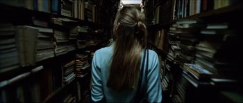 Movie still from “Bleeder” (1999), directed by Nicolas Winding Refn – A woman is walking through a library filled with lots of books; Close Up shot, Overhead angle