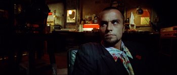 Movie still from “Bleeder” (1999), directed by Nicolas Winding Refn – A person sitting in a chair wearing a suit; Close Up shot, Over the shoulder angle