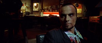 Movie still from “Bleeder” (1999), directed by Nicolas Winding Refn – A person sitting in a chair in a room; Close Up shot, Low angle