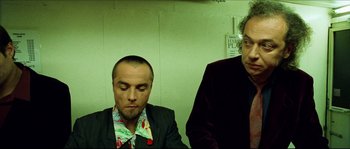 Movie still from “Bleeder” (1999), directed by Nicolas Winding Refn – Two men sitting next to each other in front of a wall; Medium shot, Low angle