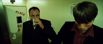 Movie still from “Bleeder” (1999), directed by Nicolas Winding Refn – A man drinking from a white cup while sitting next to another man; Medium shot, Low angle