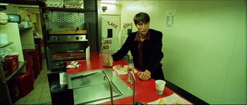 Movie still from “Bleeder” (1999), directed by Nicolas Winding Refn – A man sitting at a table in front of some food; Medium shot, High angle