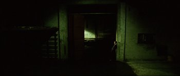 Movie still from “Bleeder” (1999), directed by Nicolas Winding Refn – A man standing in a dark room next to an open door; Extreme Wide shot, High angle