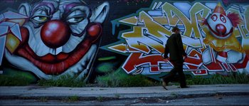 Movie still from “Bleeder” (1999), directed by Nicolas Winding Refn – A man walking down the sidewalk near a graffiti wall; Wide shot, Low angle
