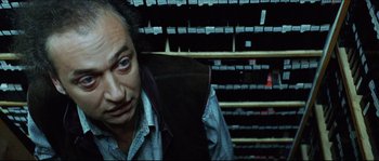 Movie still from “Bleeder” (1999), directed by Nicolas Winding Refn – A man sitting in front of a shelf filled with boxes; Close Up shot, Low angle