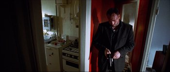 Movie still from “Bleeder” (1999), directed by Nicolas Winding Refn – A man holding a gun while standing next to a stove; Medium shot, Low angle
