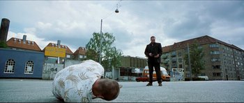 Movie still from “Bleeder” (1999), directed by Nicolas Winding Refn – A man standing next to another man on a street; Wide shot, Low angle