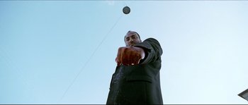 Movie still from “Bleeder” (1999), directed by Nicolas Winding Refn – A man in a black suit is throwing a frisbee; Medium shot, Low angle
