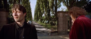 Movie still from “Bleeder” (1999), directed by Nicolas Winding Refn – A man walking down a street past a gate; Close Up shot, Over the shoulder angle