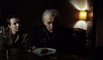 Movie still from “Blind Chance” (1987), directed by Krzysztof Kieslowski – An older man sitting at a table with a plate of food; Medium shot, Over the shoulder angle