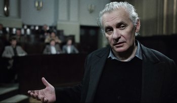 Movie still from “Blind Chance” (1987), directed by Krzysztof Kieslowski – An older man in a black jacket is in a court room; Medium shot, Low angle