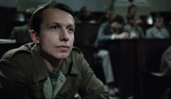 Movie still from “Blind Chance” (1987), directed by Krzysztof Kieslowski – A man sitting in front of a group of people in a room; Close Up shot, Low angle