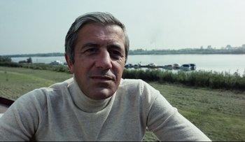 Movie still from “Blind Chance” (1987), directed by Krzysztof Kieslowski – An older man wearing a white sweater sitting in front of a body of water; Close Up shot, Low angle
