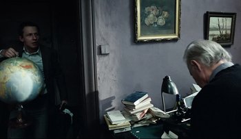 Movie still from “Blind Chance” (1987), directed by Krzysztof Kieslowski – An older man sitting at a desk with a stack of books; Medium shot, Over the shoulder angle