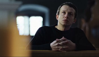 Movie still from “Blind Chance” (1987), directed by Krzysztof Kieslowski – A man sitting at a table with his hands clasped together; Medium shot, Low angle