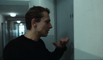 Movie still from “Blind Chance” (1987), directed by Krzysztof Kieslowski – A man in a black shirt standing in front of a wall; Close Up shot, Over the shoulder angle