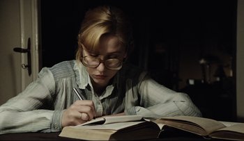Movie still from “Blind Chance” (1987), directed by Krzysztof Kieslowski – A woman is writing on a book while sitting at a table; Medium shot, Low angle