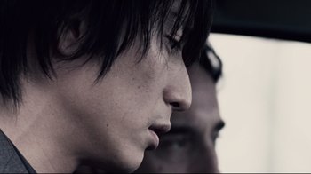 Movie still from “Blindness” (2008), directed by Fernando Meirelles – A young man's face with another young man's face in the background; Close Up shot, Over the shoulder angle