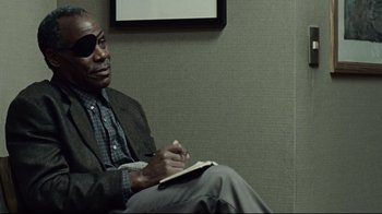 Movie still from “Blindness” (2008), directed by Fernando Meirelles – A man sitting in front of a wall holding a notebook; Close Up shot, Over the shoulder angle