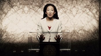 Movie still from “Blindness” (2008), directed by Fernando Meirelles – A woman standing at a podium in front of an audience; Medium shot, Low angle