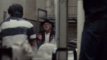 Movie still from “Blindness” (2008), directed by Fernando Meirelles – An older man in a black hat is talking to people; Medium shot, Over the shoulder angle