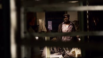 Movie still from “Blindness” (2008), directed by Fernando Meirelles – A man standing in front of a window with clothes hanging on a rack behind bars; Medium shot, Over the shoulder angle